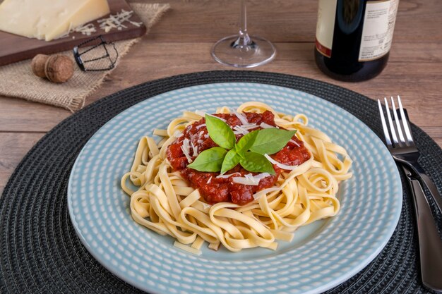 Plato con fideos cubiertos con salsa de tomate, con una copa de vino tinto espumoso.