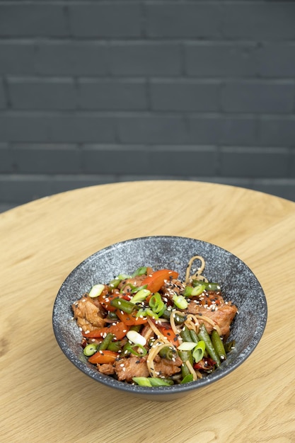 Un plato de fideos udon, ternera y verduras fritas en la mesa de madera