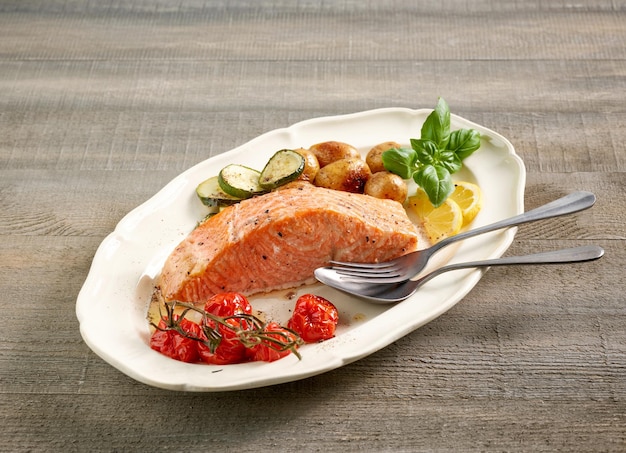 Plato de filete de salmón asado y verduras en la mesa de la cocina de madera