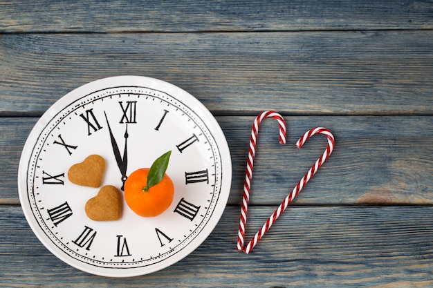 Foto un plato en forma de reloj, en el que se encuentra una mandarina y dos galletas en forma de corazón