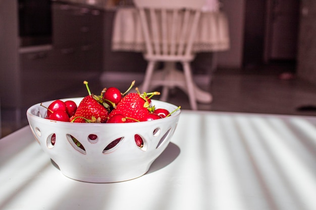 Un plato de fresas y cerezas sobre una mesa blanca en el salón