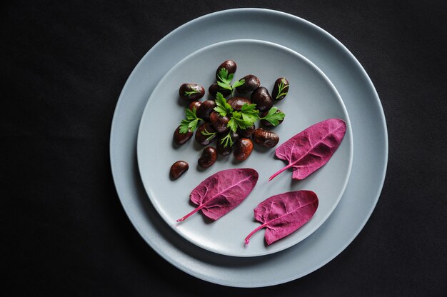 Un plato con frijoles oscuros y hojas de espinacas rojas sobre un fondo oscuro.