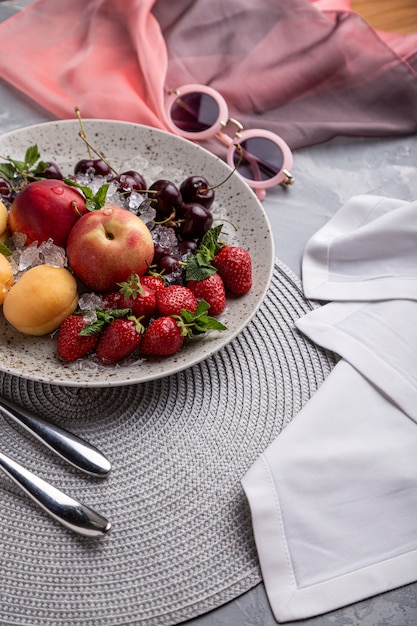 Plato de fruta saludable, fresas, manzanas, duraznos, albaricoques en una mesa de madera gris oscuro, vista superior, primer plano, enfoque selectivo.