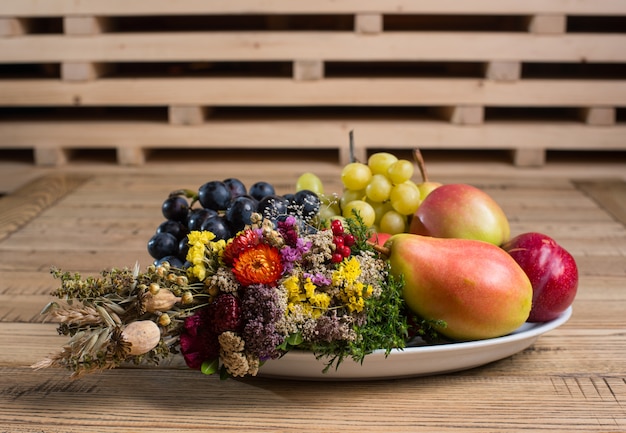 Plato de frutas con decoraciones de flores silvestres en la mesa de madera