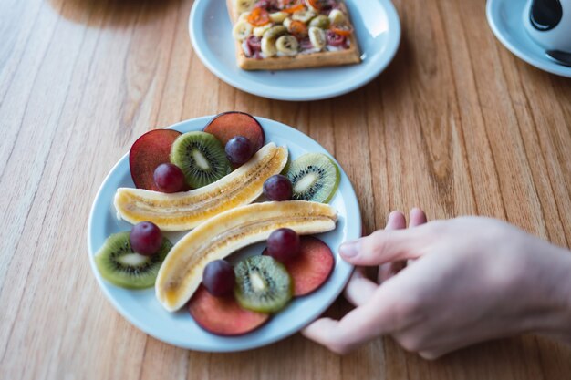 Plato con frutas frescas en una mesa de madera - Desayuno o postre saludable con ciruelas, uvas, plátanos y kiwi.
