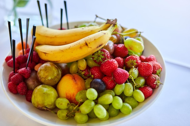 Plato con frutas frescas y sabrosas como plátanos fresas uvas melocotones y peras Comida vegetariana Tazón de bayas mixtas sobre la mesa