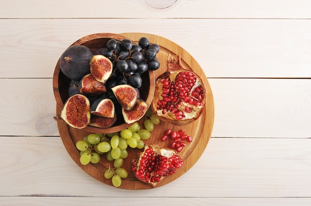 Plato de frutas con higos, uvas, granada sobre superficie de madera