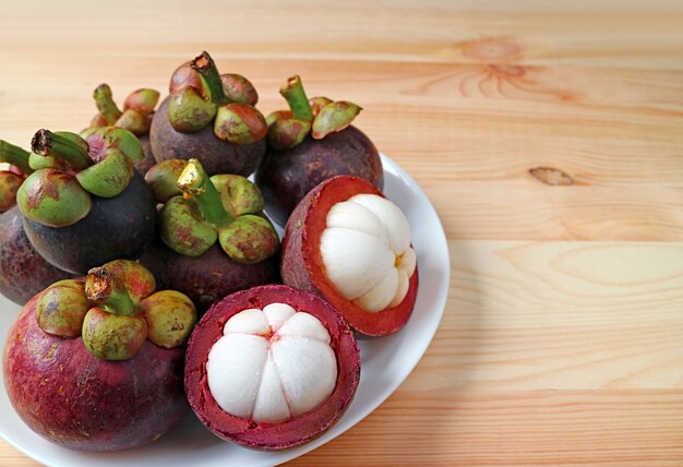 Plato de frutas de mangostán maduras con un par de frutas cortadas mostrando la deliciosa carne blanca