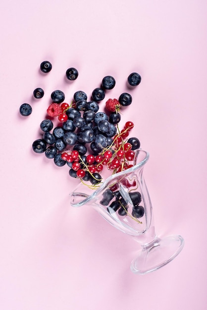 Un plato de frutas de verano sobre unas gafas de fondo rosa de las que se dispersan las bayas