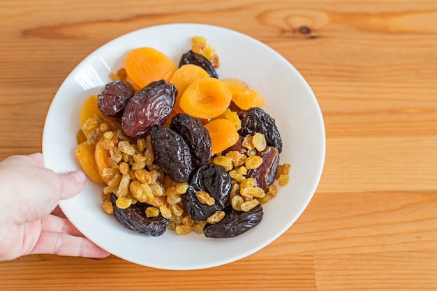 Plato con frutos secos sobre una mesa de madera. Alimentos útiles: dátiles, orejones, ciruelas pasas, pasas