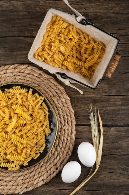 Plato de fusilli crudo y huevos crudos sobre superficie de madera.