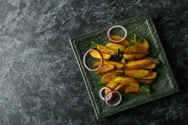 Plato con gajos de patata, perejil y cebolla sobre ahumado negro