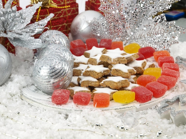 Un plato de galletas con una bola plateada y un árbol de navidad plateado al fondo.