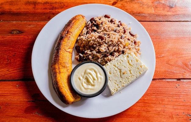 Plato de gallopinto con queso y maduro sobre mesa de madera Concepto de comida nicaragüense Comida tradicional de Gallo Pinto con maduro y queso servido