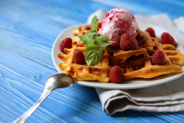 Plato de gofres belgas con helado y bayas frescas sobre fondo de madera azul vista superior