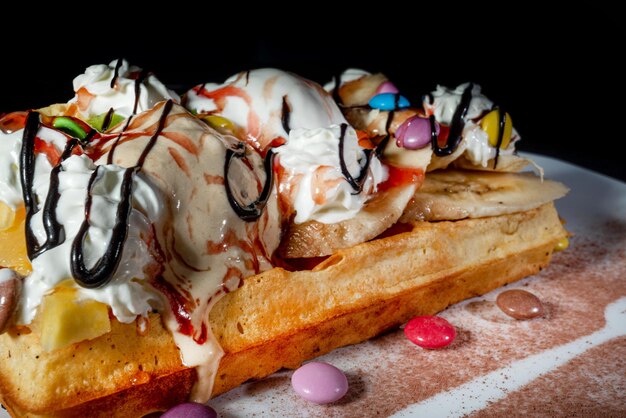 Foto plato de gofres belgas con salsa de caramelo de helado y bayas frescas sobre fondo oscuro