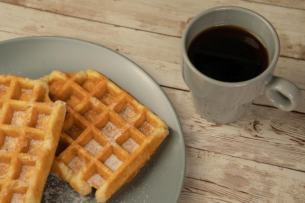 Plato con gofres recién horneados con una taza de café negro sobre un fondo de madera clara concepto de pastelería para el desayuno