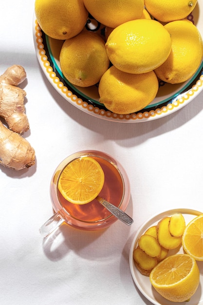 Plato grande con limones y una taza de té y una raíz de jengibre sobre una mesa cubierta con un mantel blanco