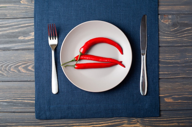 Foto plato gris con chile pimiento rojo, cuchara y cuchillo con mantel de lino azul sobre la mesa