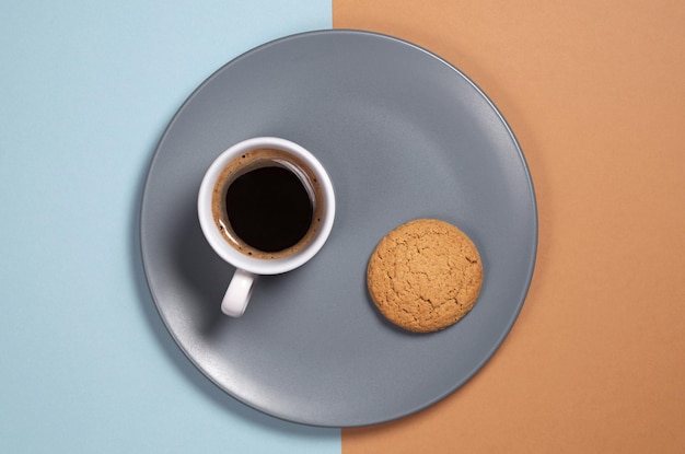 Plato gris con taza de café y galleta de avena sobre un fondo de dos colores, vista superior
