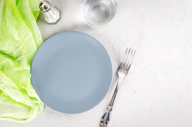 Plato gris vacío que sirve para la cena y cubiertos sobre fondo de hormigón gris.