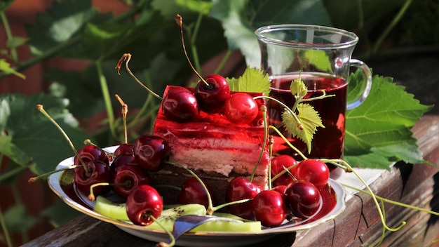 En el plato hay un trozo de pastel, muchas cerezas y rodajas de kiwi y un vaso de jugo de cereza.