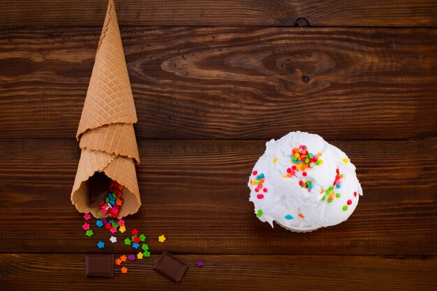 Plato de helado de vainilla scoop swith sprinkles y conos de waffle en madera.