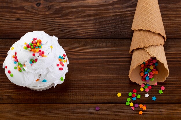 Plato de helado de vainilla scoop swith sprinkles y conos de waffle sobre fondo de madera con espacio de copia.