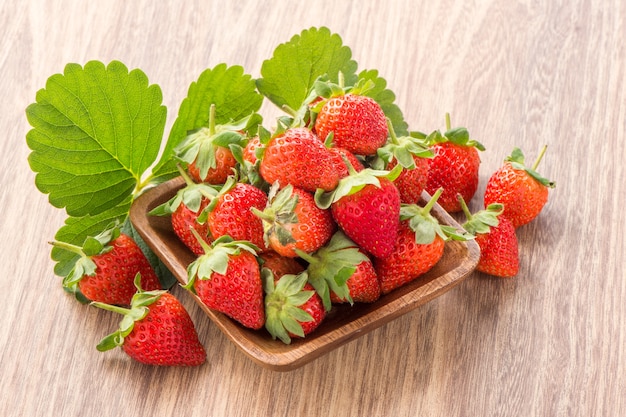 Un plato de hermosas fresas aislado sobre fondo de madera, de cerca.