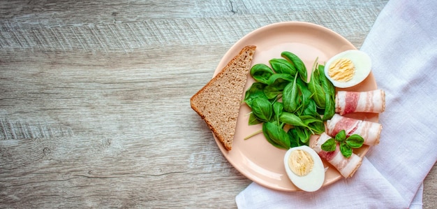 Plato con hojas de espinaca albahaca verde tocino huevos y un trozo de pan de centeno Comida para el desayuno