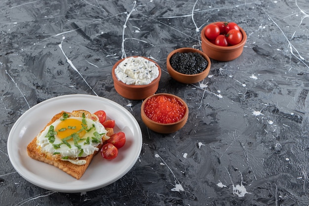 Plato de huevo frito tostadas, crema agria y caviar en mesa de piedra.