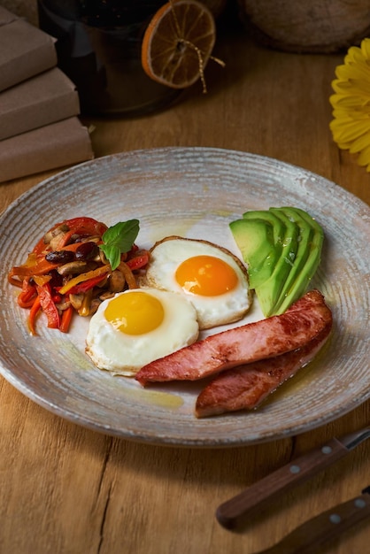 Plato de huevos fritos con tocino y aguacate en la mesa de madera Desayuno inglés en la mesa