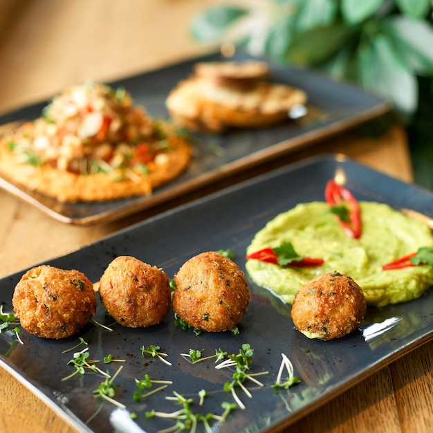 Plato de hummus de garbanzos y guacamole y falafel en placa azul sobre una mesa de madera