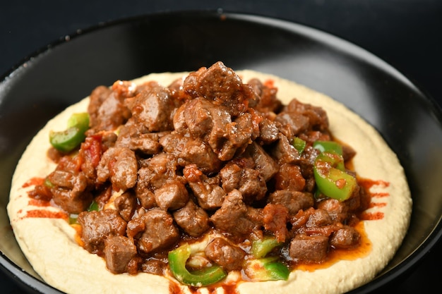 Un plato de hummus con salsa roja y pimientos verdes encima.