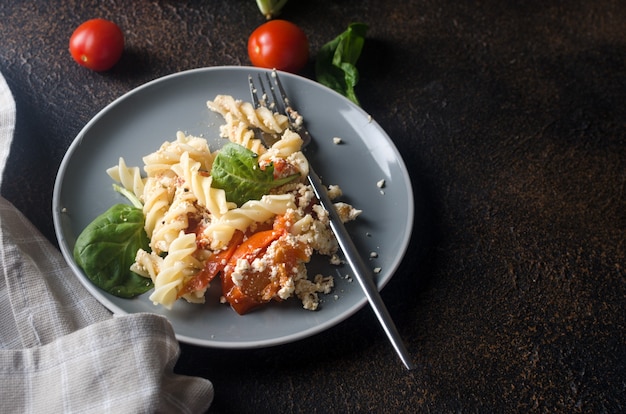 Plato italiano de pasta mezclada con queso feta al horno y tomates sobre un fondo oscuro. Fetapasta. Receta viral de tendencia, plano, espacio de copia