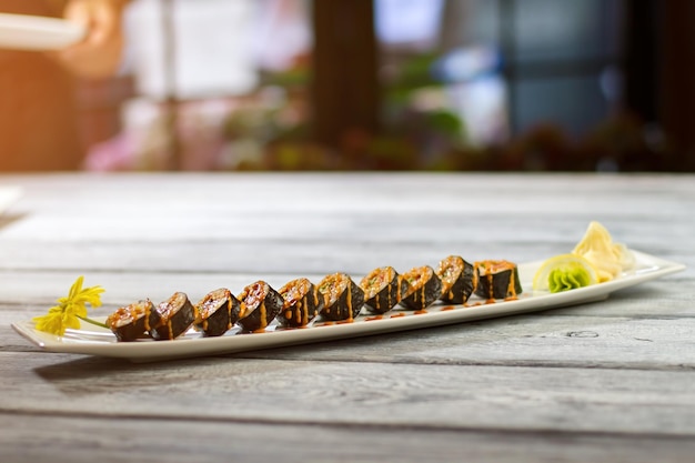 Plato largo con rollos de sushi. Plato de sushi sobre superficie de madera. Deliciosa comida baja en calorías. Rollos de Hosomaki y jengibre marinado.