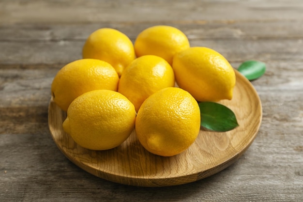 Plato con limones frescos y hojas sobre mesa de madera