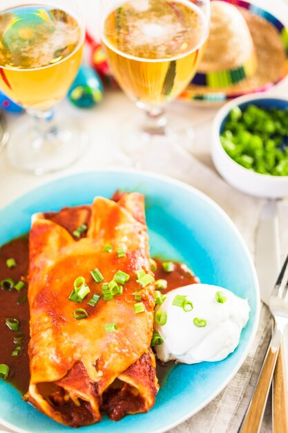 Plato llano con enchiladas de pollo aderezado con cebollas verdes y crema agria.