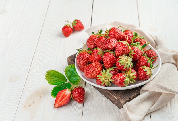 Un plato lleno de fresas maduras sobre un soporte de madera sobre un fondo claro