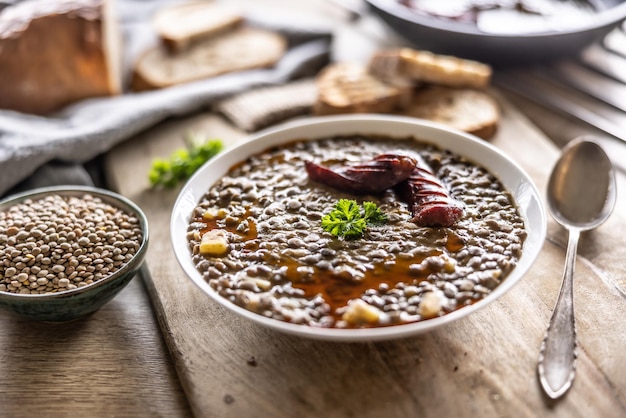 Un plato lleno de sopa de legumbres de lentejas con salchicha al horno y pan fresco