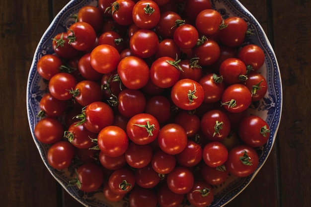 Plato lleno de tomates cherry maduros en una mesa de madera a la luz del sol