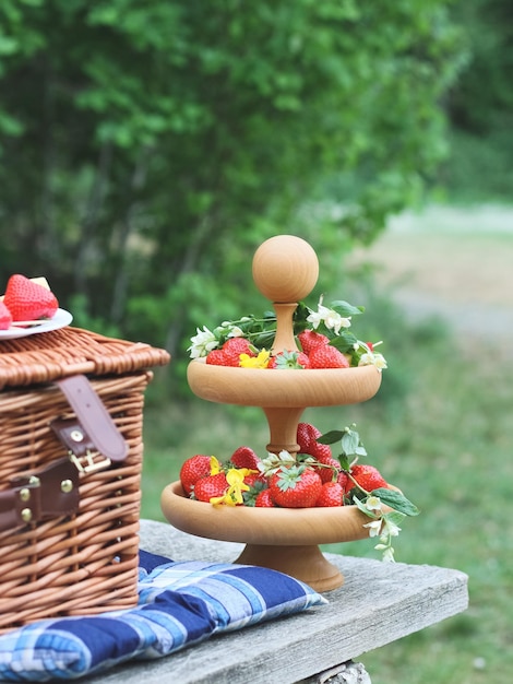 Un plato de madera de dos niveles con uvas de fresas rojas maduras con queso en brochetas y una cesta de picnic de mimbre