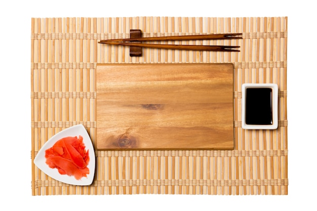 Plato de madera marrón rectangular vacío con palillos para sushi, jengibre y salsa de soja en la superficie de la estera de bambú amarillo