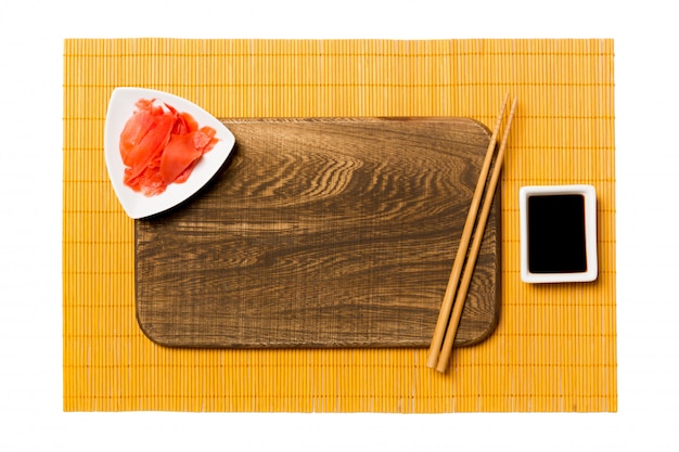 Plato de madera marrón rectangular vacío con palillos para sushi y salsa de soja en amarillo