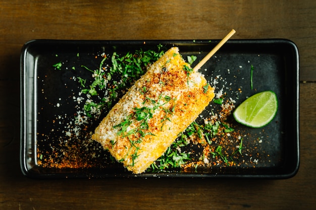 Plato de maíz a la parrilla al estilo mexicano con queso y chile en polvo servido con rodajas de limón