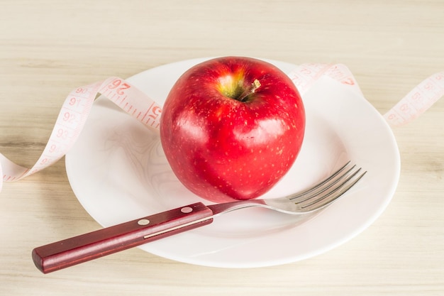 Plato con manzana y cubiertos y cinta métrica.