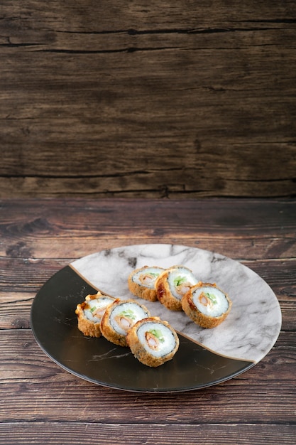 Foto plato de mármol de delicioso rollo de tempura colocado sobre superficie de madera.