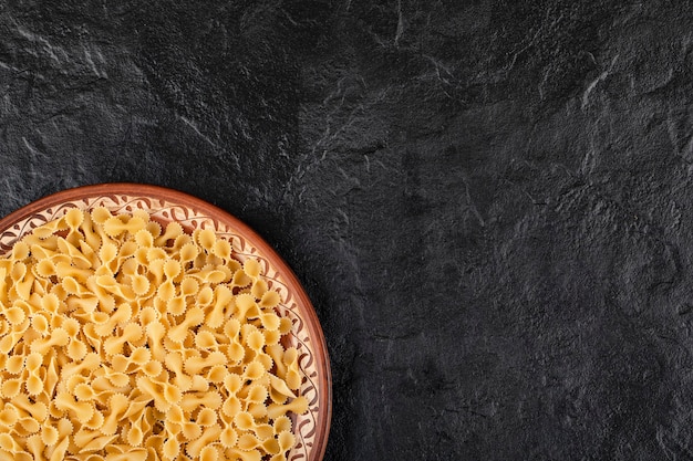 Plato marrón de macarrones crudos colocado sobre la mesa negra.