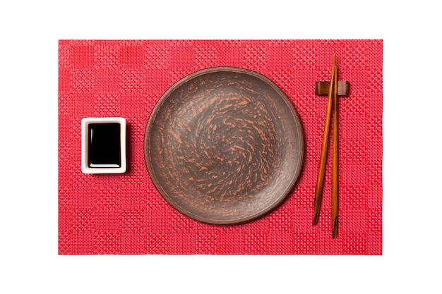 Plato marrón redondo vacío con palillos para sushi y salsa de soja sobre fondo de sushi de alfombra roja. Vista superior con espacio de copia para su diseño.