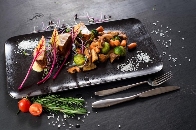 Plato de medallones de carne y verduras sobre fondo de madera negra